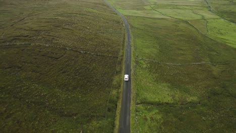 following tracking shot of single white car remotely driving down country track