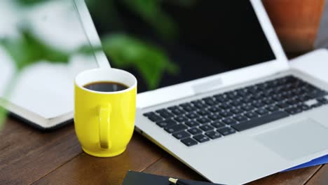 laptop, notebook and cup of coffee arranged on wooden table