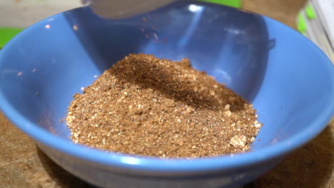 dumping brown spices in blue bowl, slow motion close up