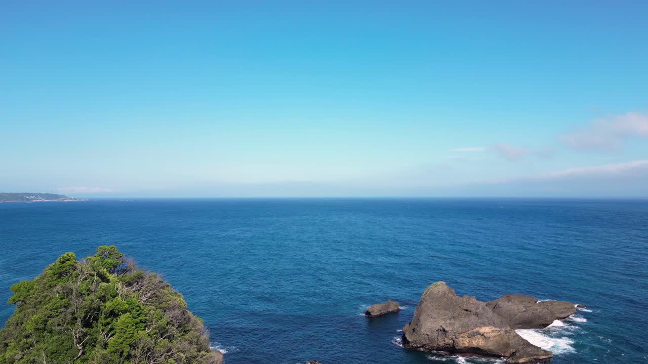 Slow cinematic drone flight over jagged rocky island in blue ocean