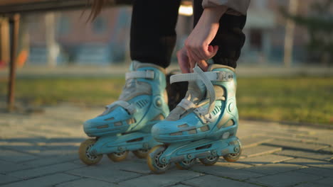 a person sitting in a park, fastening the straps on their second rollerblade while already wearing the first one. moments of preparation before engaging in a rollerblading activity