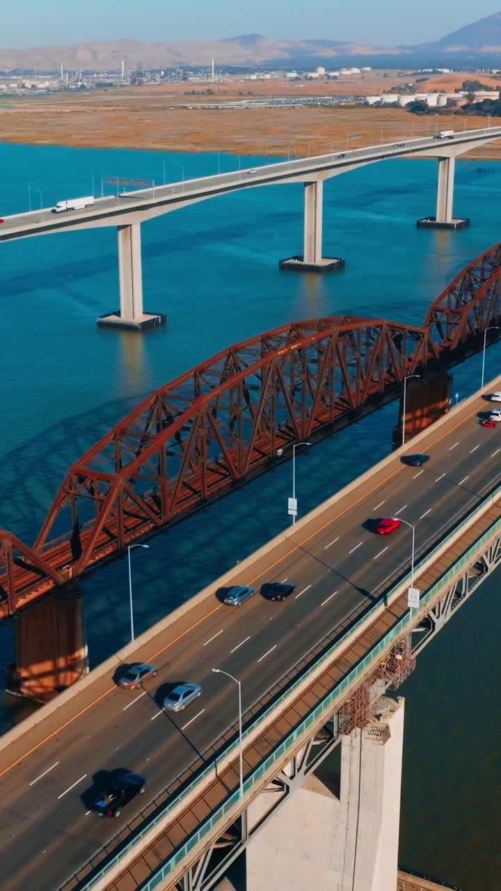 Sunny day footage over the bridges connecting Martinez to Benicia, California, USA. Multiple cars moving by the bridges. Mountainous landscape at backdrop. Vertical video