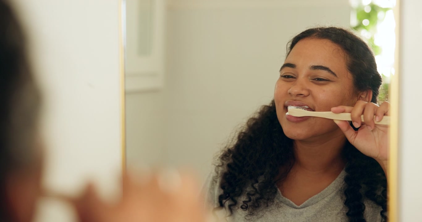 Young Woman Brushing Teeth in Front of Bathroom Mirror