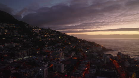 Forwards-fly-above-evening-city.-Residential-buildings-and-hotels-in-tourist-destination-at-sea-coast-against-sunset-sky.-Cape-Town,-South-Africa