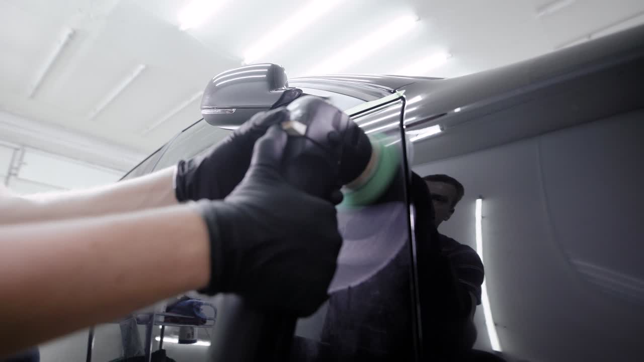 노동자는 자동차 염료에 보호 커버를 만들고, 오토 서비스에서 회전 는 기계로 마사지합니다.