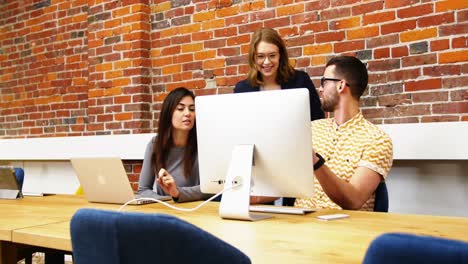 Group-of-executives-discussing-over-computer-at-desk