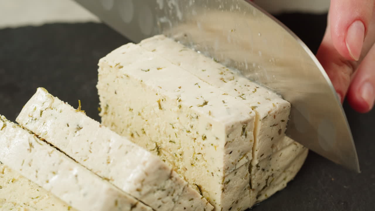Chef cut cheese for Fried tofu with sesame seeds and spices on cast iron pan, cooking japanese salad. Healthy ingredient for cooking vegan vegetarian diet food. Roasted tofu over black background.