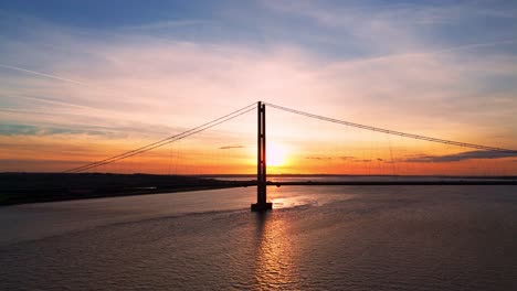 The-Humber-Bridge,-kissed-by-the-setting-sun,-comes-to-life-as-an-aerial-drone-captures-a-tranquil-ballet-of-cars-beneath