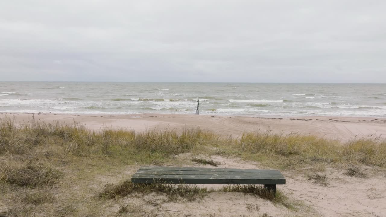 establecimiento de una vista aérea de la costa del mar báltico en un día nublado, enmarcar jurmalciems, antiguo muelle de madera, playa de arena blanca, grandes olas de tormenta aplastando la costa, disparos de drones avanzando