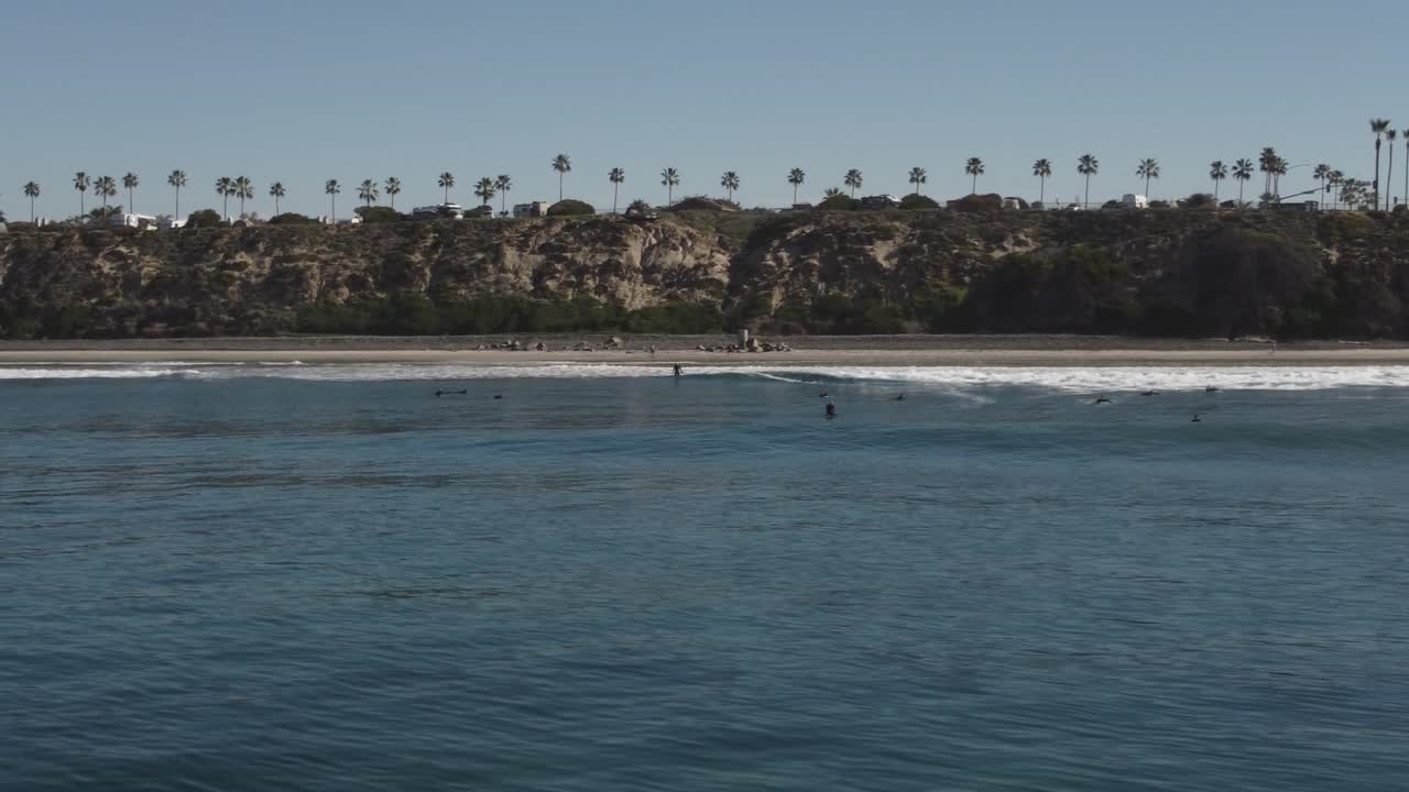 아름다운 공중 드론 샷, 해안을 따라 물 위로 낮게 날아가는 드론, 두 명의 서퍼, 칼즈배드 주립 해변 - 캘리포니아