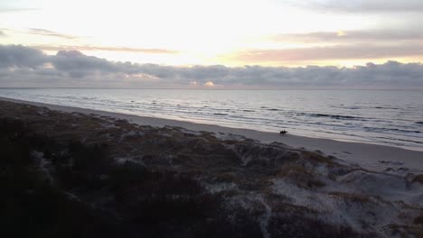 aerial drone flyover perkone sandy beach baltic sea coastline, two horse riders at the beach after the sunset, no people, autumn, spring, moving forward over the dunes, relieving shot over the dunes