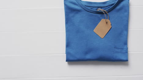 video of flat lay of blue t shirt with tag and copy space on white background