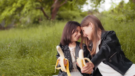 two happy sisters eating bananas in a park