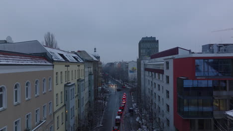 Fly-over-queue-of-cars-stopping-at-traffic-lights-on-road-intersection.-Winter-city-at-dusk.-Berlin,-Germany