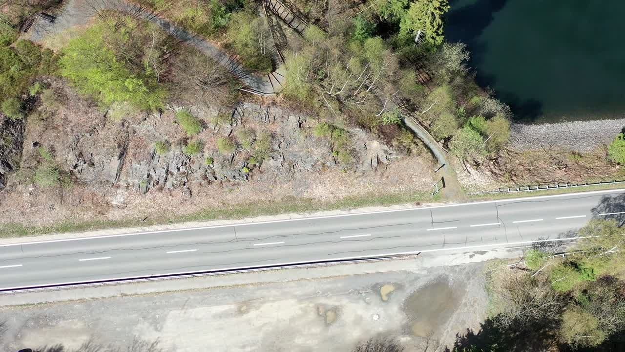 Aerial photograph of an arc-shaped flight over an asphalted country road with an embankment on which the raw rock of carbonaceous clay slate spreads out