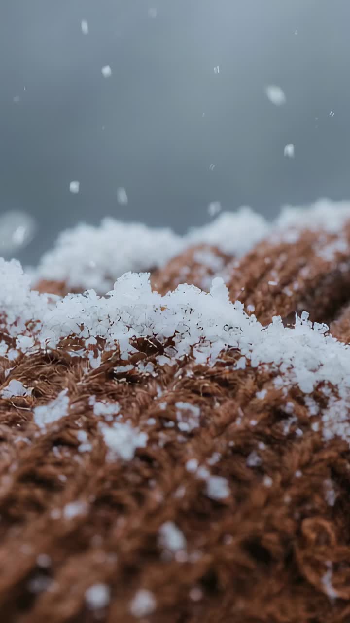 Vertical video: Drifting snow settling on brown knit closeup from overcast sky, forming thin ridges