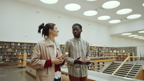 Multiethnic-Man-and-Woman-Walking-in-Library-and-Talking