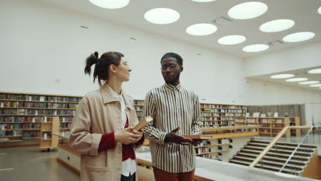 hombre y mujer multiétnicos caminando por la biblioteca y hablando