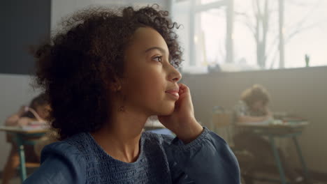 bored kid sitting at desk in classroom. thoughtful student looking at window