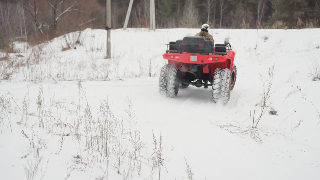 Un quad visto da dietro con le ruote che girano nella neve farinosa, spruzzi di neve esplosivi e vapore dallo scarico mentre il pilota esegue una curva stretta attraverso un campo aperto, pneumatici chiodati sovradimensionati che lasciano nuove tracce, movimento cinetico.