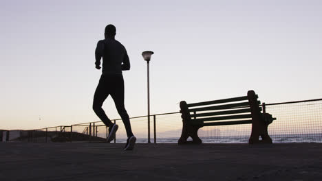 Hombre-Afroamericano-Haciendo-Ejercicio-Al-Aire-Libre,-Corriendo-Junto-Al-Mar-Por-La-Noche