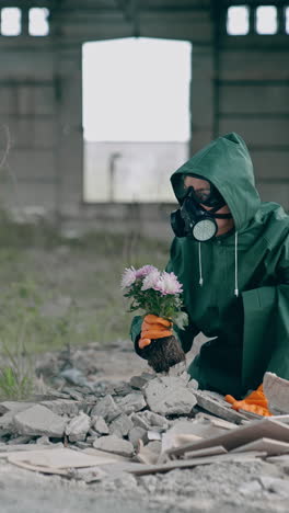 woman in safety uniform in abandoned place. scientist in protective suit and respirator with tendy flowers in ruined building. environment in danger. vertical video