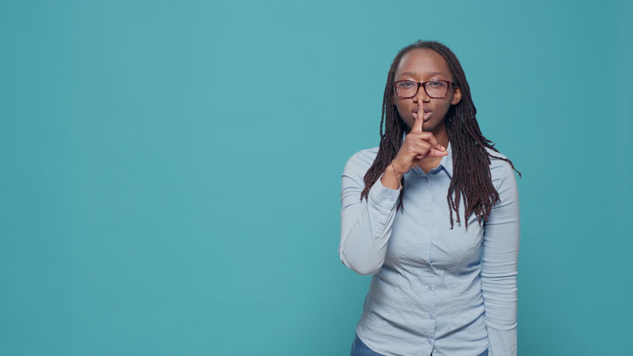 Young adult doing hush silence gesture with finger over mouth