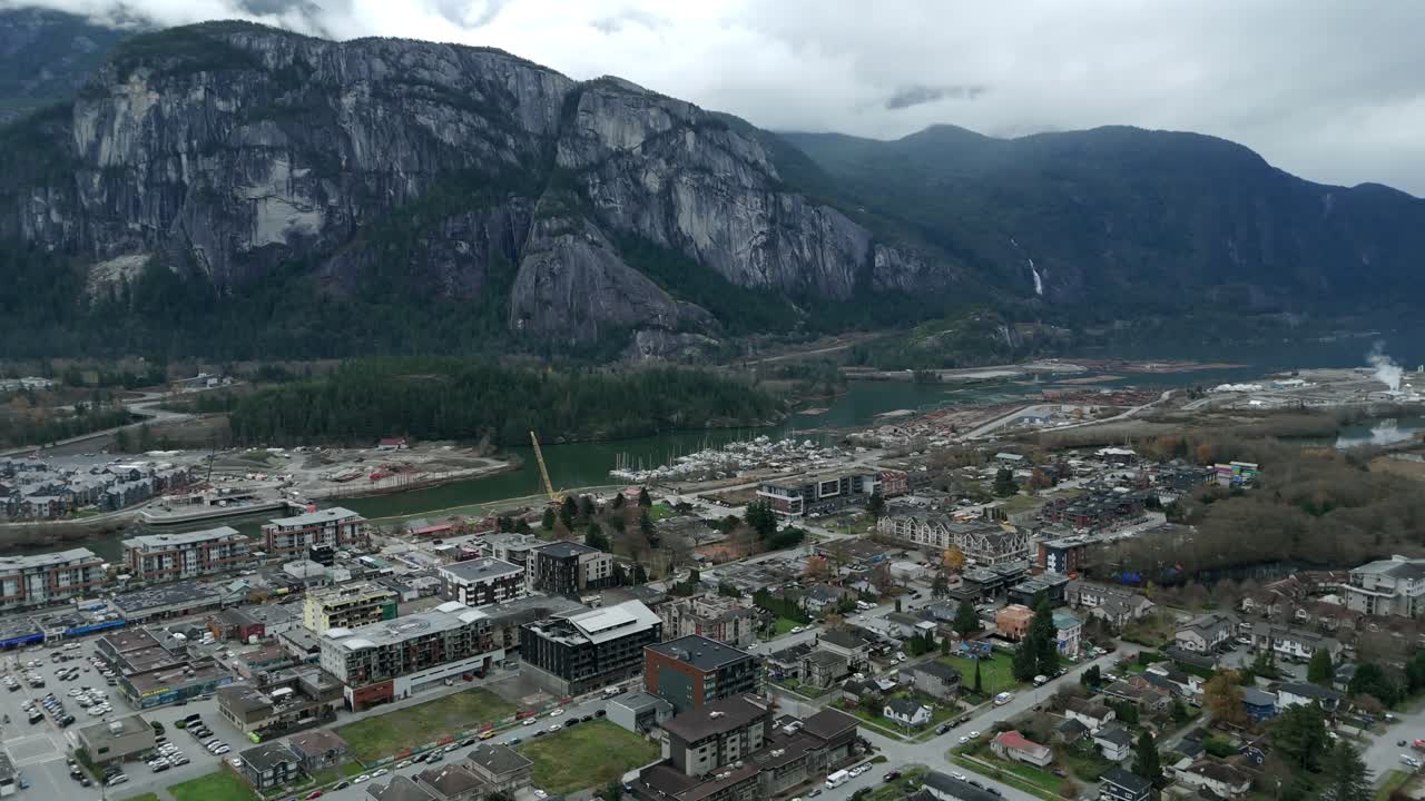 Squamish, Canada – En kompakt by breder sig ud over dalbunden, indrammet af stejle, klippefyldte bjerge og snoede vandveje under en skyet himmel – dronefoto