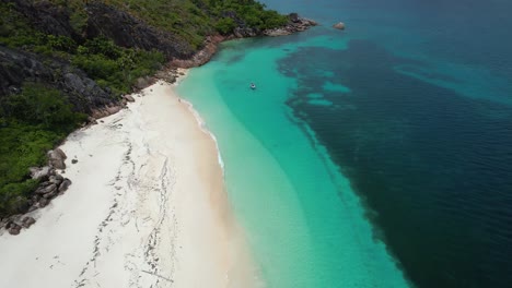 Aerial-View-of-Curieuse-Island-Seychelles-beach-with-rocky-coastline-and-boat-anchored-in-turquoise-clear-water