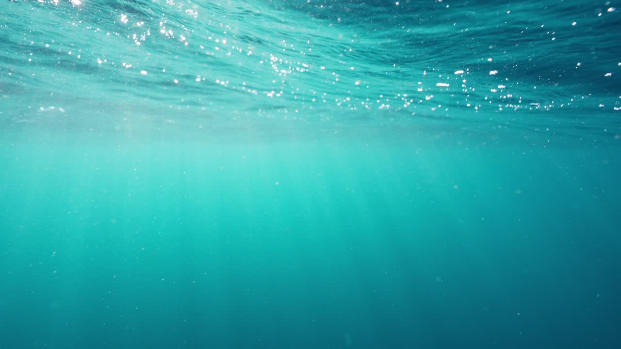 Underwater shot showing the turquoise depths and rippling surface of the ocean as the suns rays shine through