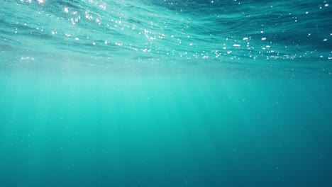 underwater shot showing the turquoise depths and rippling surface of the ocean as the suns rays shine through