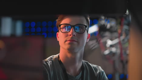 close-up of focused person in glasses working at a computer, concentrating on tasks in a studio environment, illuminated by bright background lights, with reflections in glasses