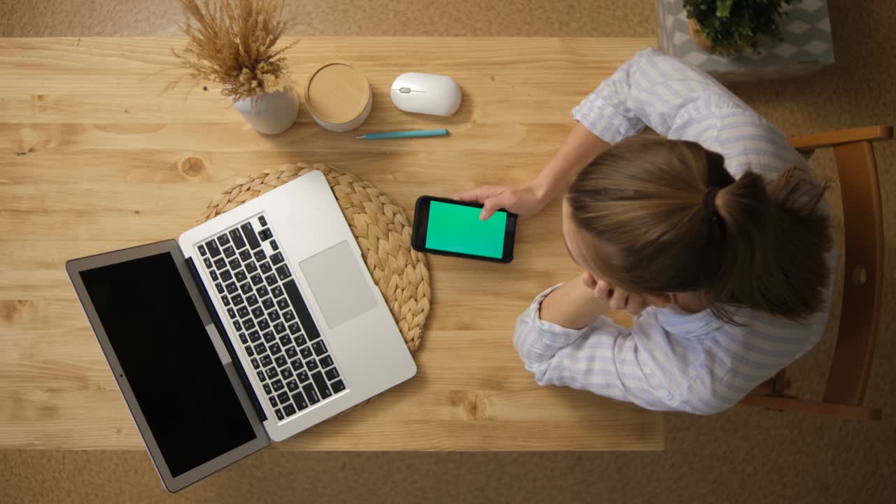 The girl is surfing on the Internet. and sits in social networks instead of remote learning. The green screen of the phone monitor. A laptop. Top view. Remote work