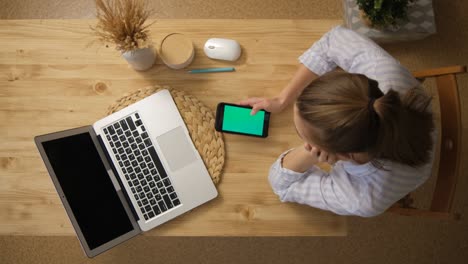the girl is surfing on the internet. and sits in social networks instead of remote learning. the green screen of the phone monitor. a laptop. top view. remote work