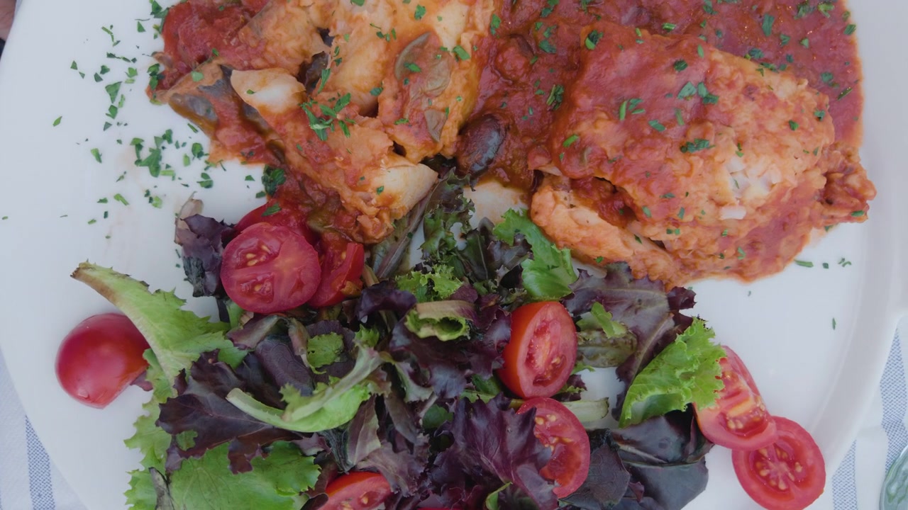 Primo piano di un filetto di pesce in salsa di pomodoro con olive accanto a un'insalata verde fresca