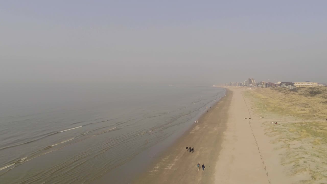 여러 그룹의 사람들이 먼 거리까지 뻗어 있는 매끄러운 모래사장을 걷고 있습니다.