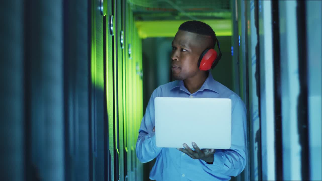 African american male computer technician using laptop working in business server room