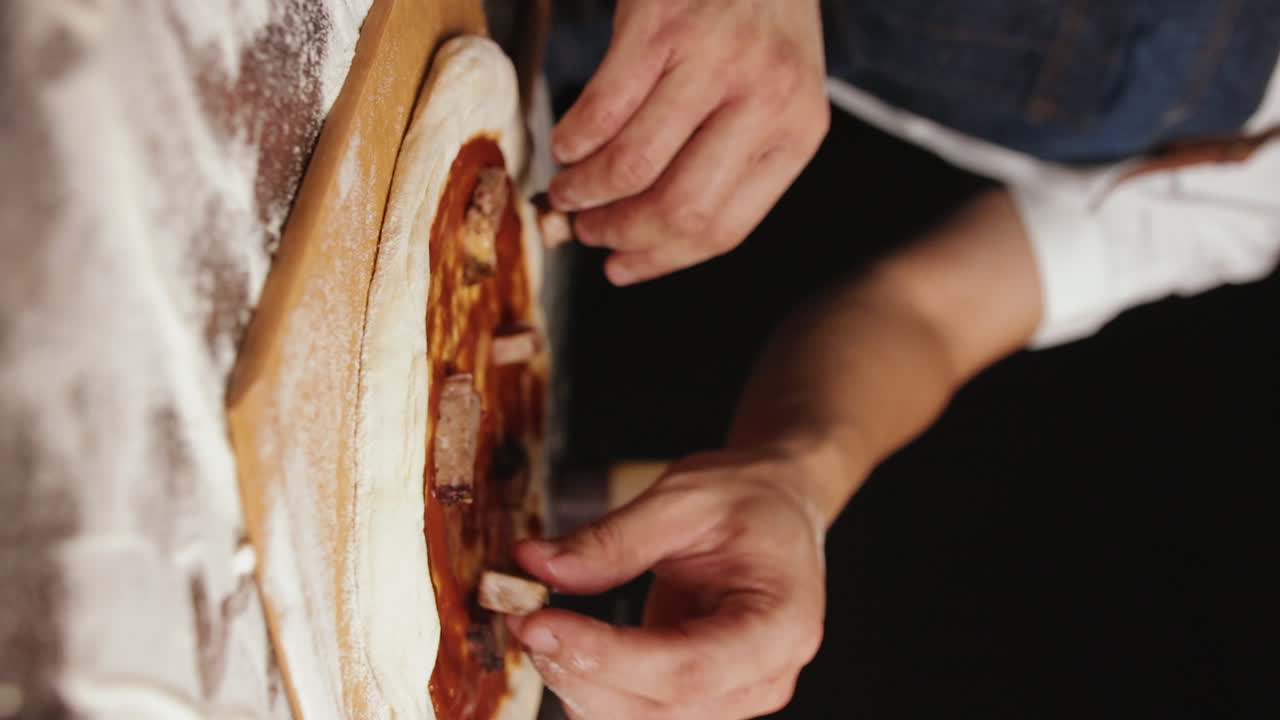 Primo piano ravvicinato delle mani di uno chef che condisce l'impasto della pizza con manzo, telecamera in movimento.