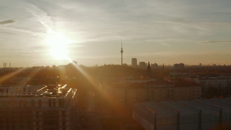 Langsamer-Absenkender-Kran-über-Wohnstraße-In-Berlin,-Deutschland-Nachbarschaft-Bei-Sonnenuntergang-Zur-Goldenen-Stunde-Und-Blick-Auf-Die-Skyline-Der-Stadt,-Luftdrohnenaufnahme