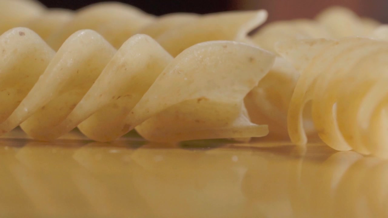 Primo piano macro di pasta fusilli cruda disposta su un tavolo di legno con profondità di campo ridotta. Pasta secca caratterizzata da forma a spirale, consistenza liscia e colore naturale per la preparazione alimentare.
