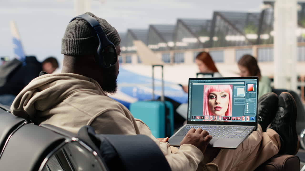 Man with Headphones Edits Photo on Laptop at Airport Terminal