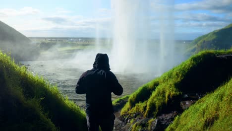 Turista-Masculino-Con-Chaqueta-Encapuchada-Con-Pintoresca-Cascada-De-Seljalandsfoss-En-El-Sur-De-Islandia