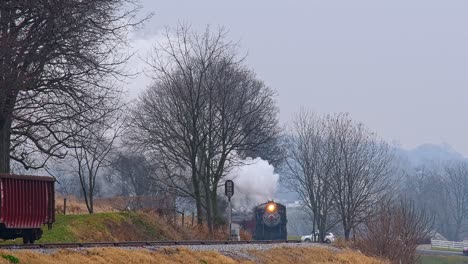 una vista a largo plazo de un tren de pasajeros de vapor que dobla una curva, que sopla humo en un día de invierno