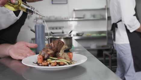 Caucasian-male-chef-pouring-olive-oil-on-meal-in-kitchen,-slow-motion