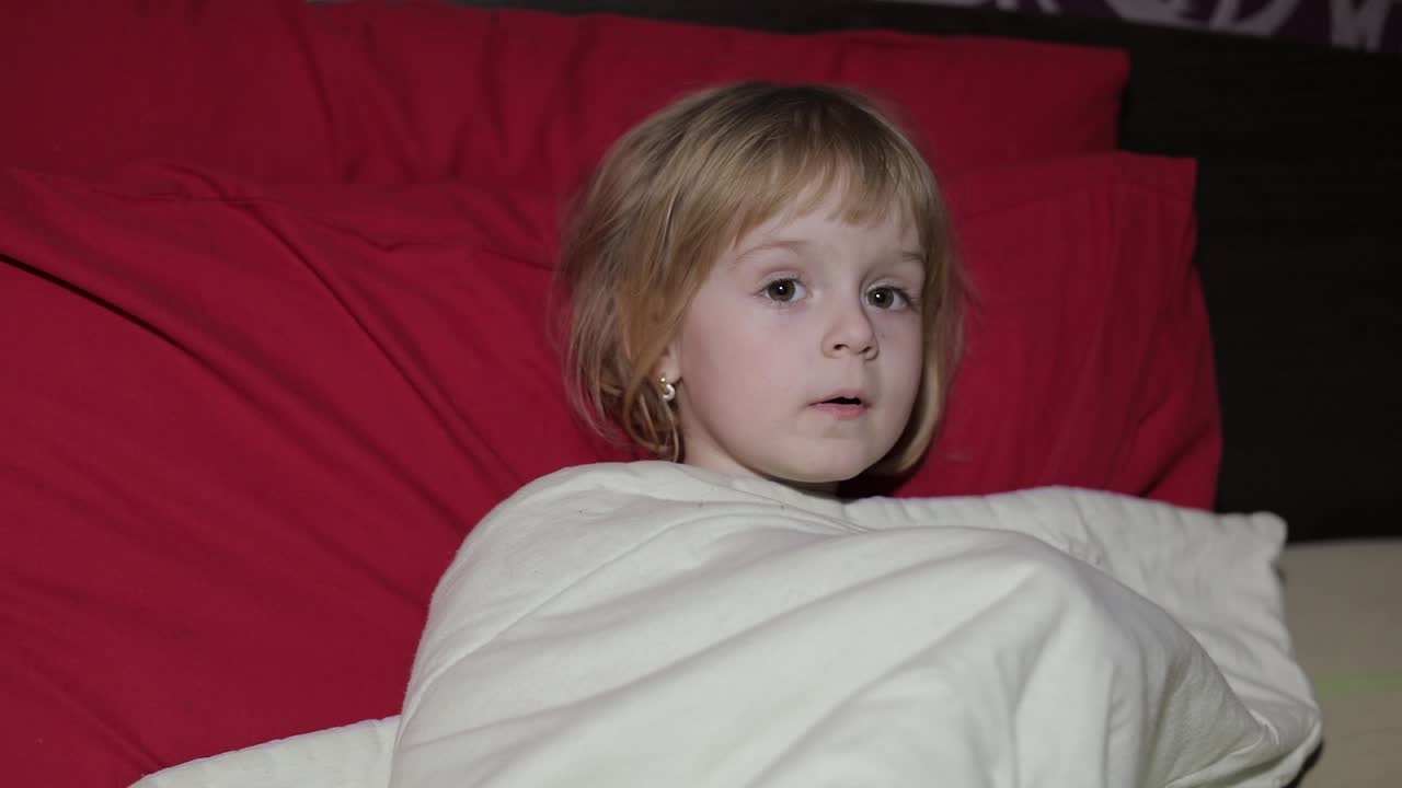 어린 소녀가 침대에 앉아 tv를 보고 있다.