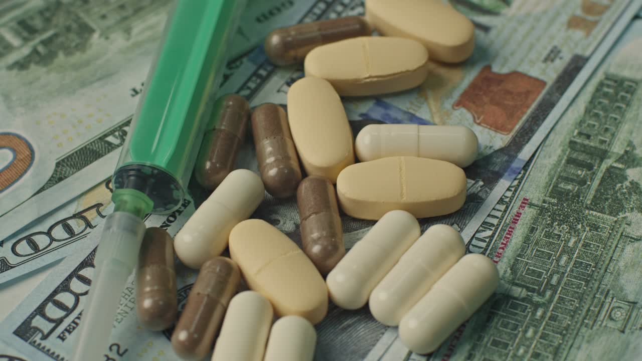 백색 의약품과 주사기가 미국 달러에 회전하는 클로즈업 뷰 - 의료의 증가하는 비용 - 제약 산업, 의학, 중독 개념