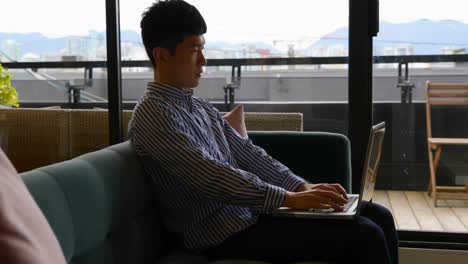 Side-view-of-young-Asian-businessman-working-on-laptop-in-modern-office-4k