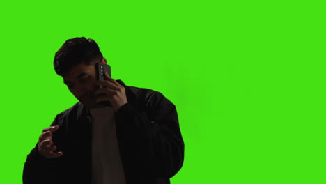 Young-Man-Talking-On-Mobile-Phone-Standing-Against-Green-Screen-Studio-Background-With-Low-Key-Lighting-1