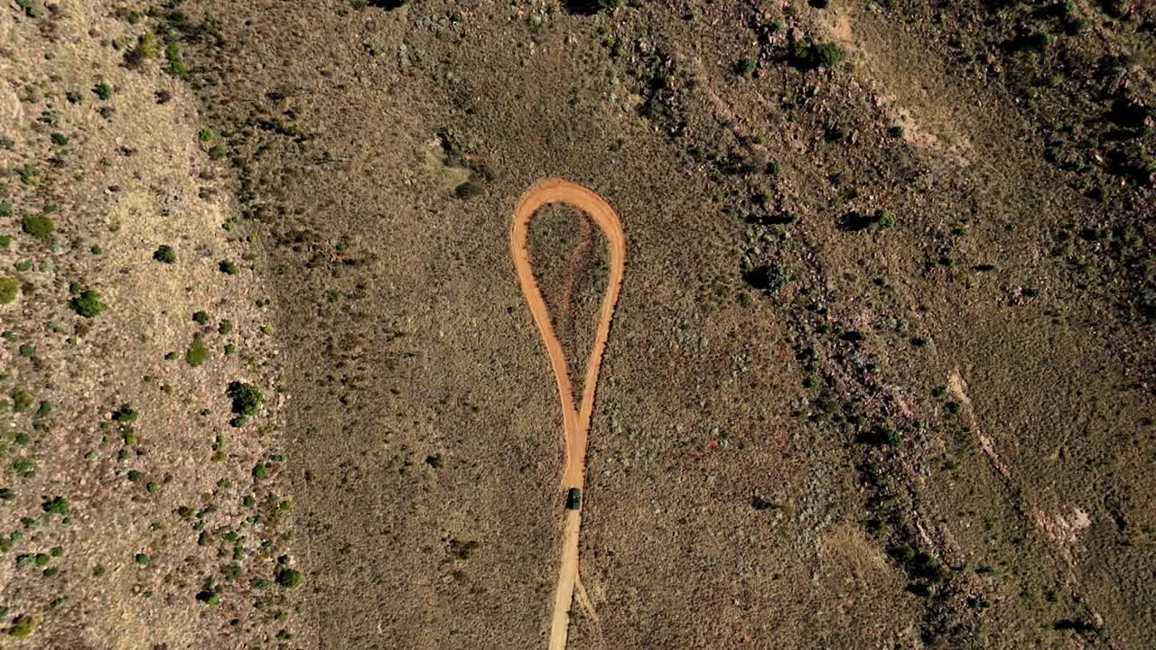 Vehicle on a dusty road, drone shot, heading to a vast rocky landscape, dead end ahead with a circle in the road - outdoor adventure through remote rugged wilderness