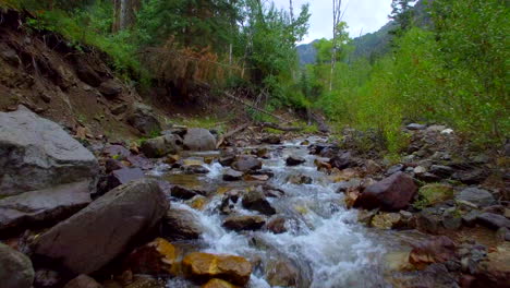 Low-flying-drone-shot-over-a-peaceful-flowing-creek-towards-some-green-trees